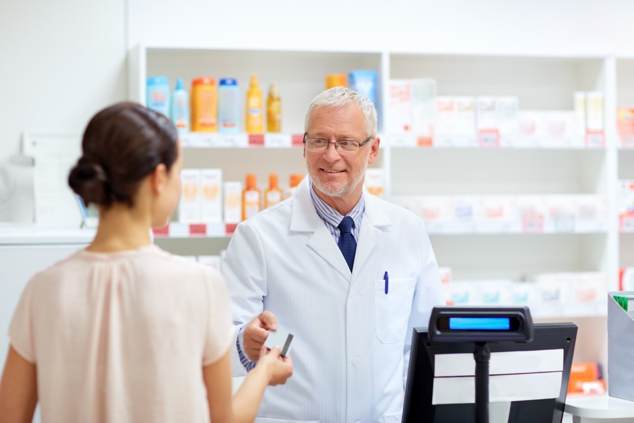 medicine, healthcare and people concept - smiling senior apothecary taking credit card from customer at pharmacy cash register