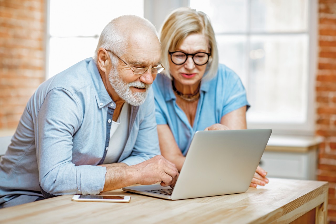 Senior couple in blue shirts feeling happy, sitting together with laptop at home