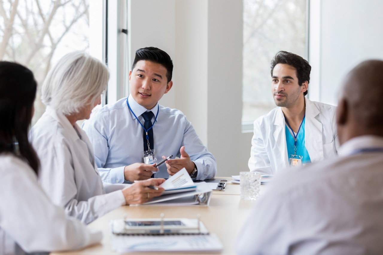 Mid adult male hospital administrator gestures while discussing hospital business with a female doctor during a staff meeting.