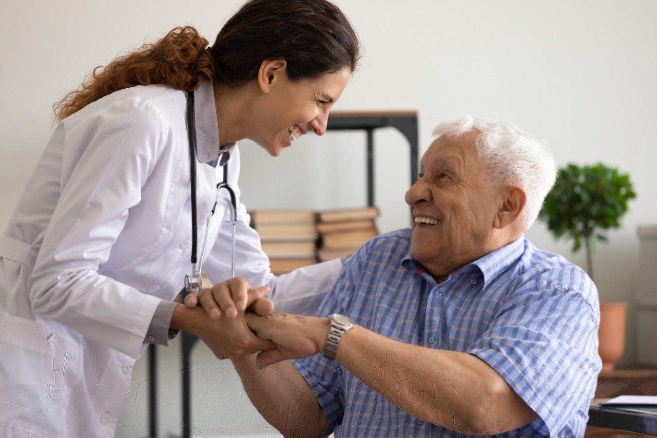 Overjoyed young Caucasian female doctor support laugh have fun with old 80s patient in clinic. Smiling woman nurse comfort caress mature elderly man client in hospital show good medical service.